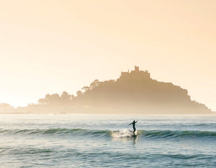 Surfer riding wave in front of St Michaels Mount