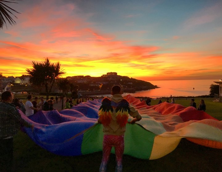 A large rainbow flag is held aloft at sunset