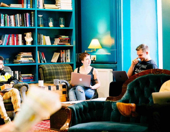 Falmouth University students sat on sofas in a blue room with bookshelves