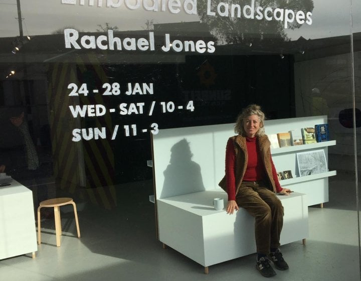A woman sitting on a white sofa behind a large glass gallery window