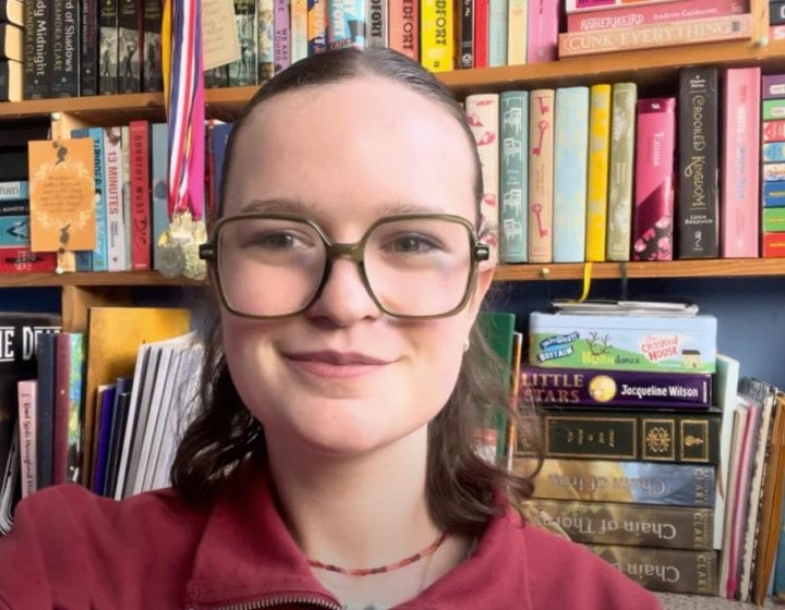 A Falmouth University student smiling at the camera, behind a book case
