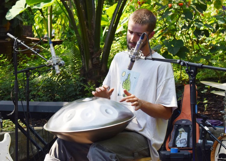 A young man playing a metal instrument surrounded by plants
