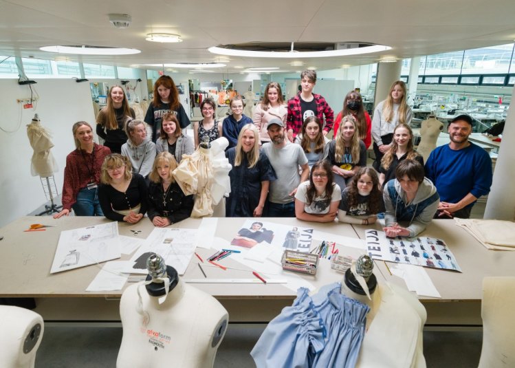A group of teenagers showcase their artwork - sketches and mannequins with clothing are visible 
