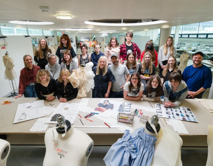 A group of teenagers showcase their artwork - sketches and mannequins with clothing are visible