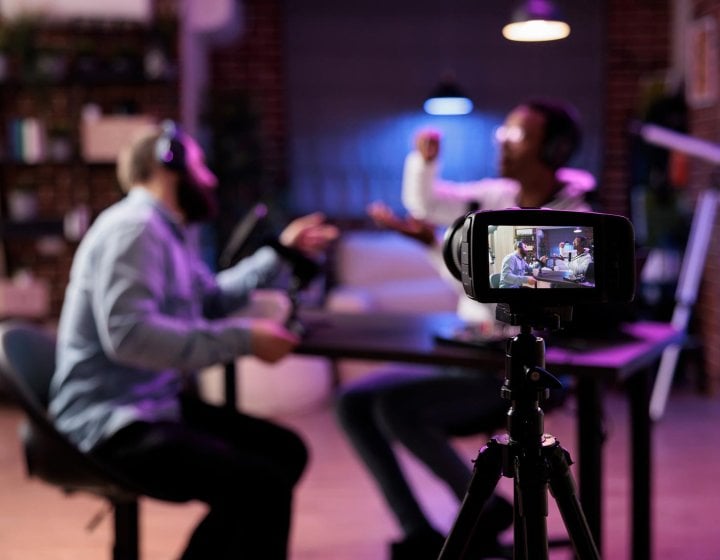 View of SLR camera filming two people in conversation around a table