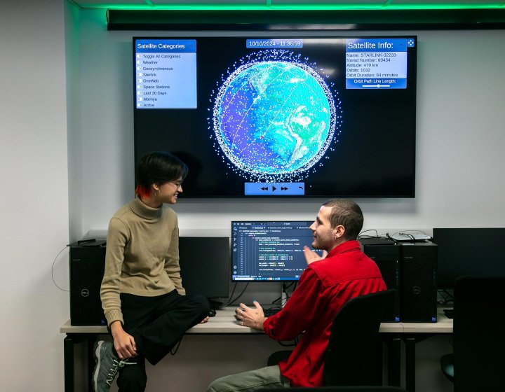 Two software engineering students in discussing with large screen of the world on the wall