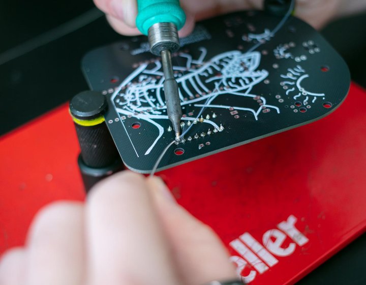 Hands using a soldering iron under a lamp