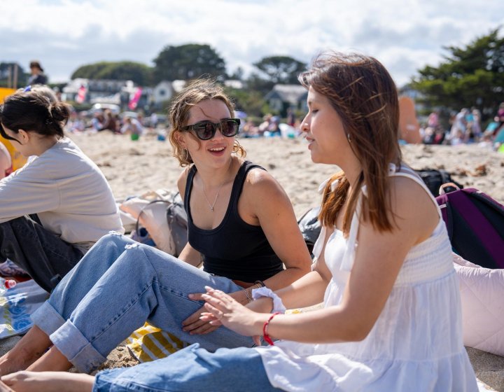 Two Falmouth University students sitting on a beach in the sun