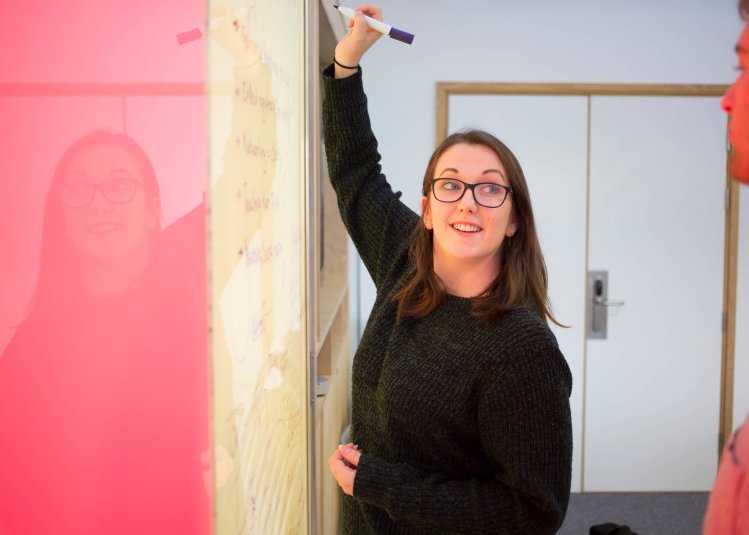 Student writing on a vibrant pink and yellow wall board, Falmouth University