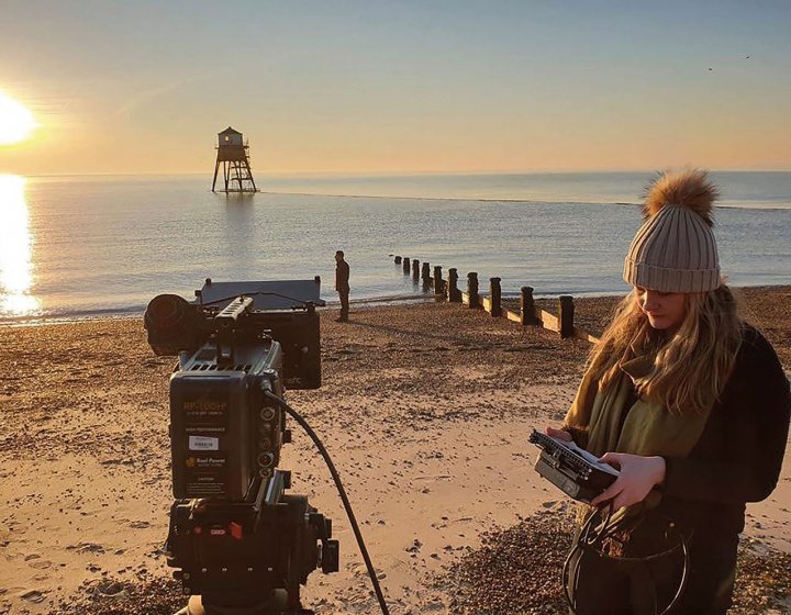 Student with film camera on beach at sunrise