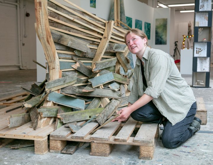 A Fine Art student kneeling by her wooden boat installation