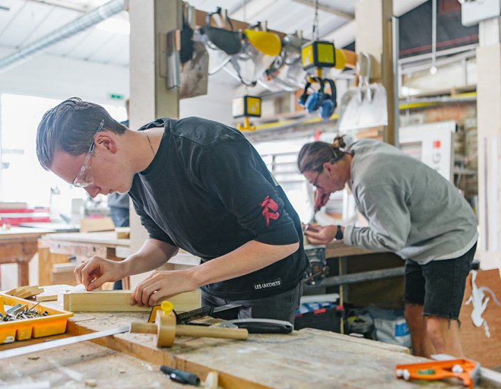 A couple of people working with wood at workshop benches