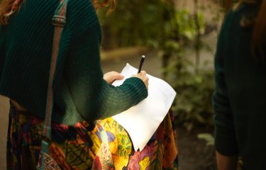 A girl in a green jumper writing on white paper