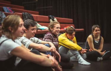 Group of students sat on theatre floor and smiling.