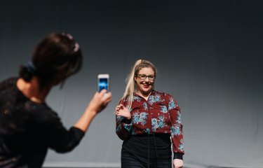 A student smiling while being filmed on a phone by another student