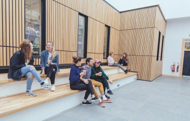 Falmouth University students sitting on steps with a wooden cladded wall behind