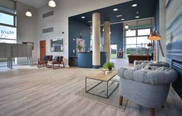 Modern open plan living area with grey armchair, wood flooring and large columns