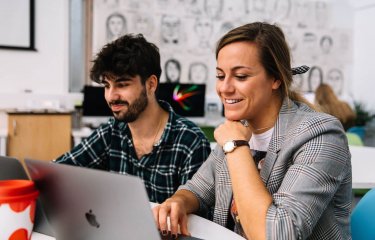 Two Falmouth University Creative Advertising students smiling at a laptop