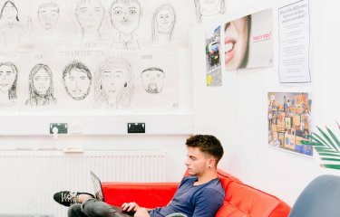 Male Creative Advertising student sitting on a red sofa at Falmouth University