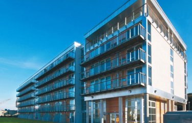 five-storey apartment building with glass balconies, grass and blue sky