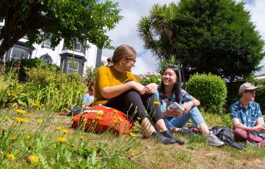 Falmouth University students sat and chatting in gardens on Falmouth Campus