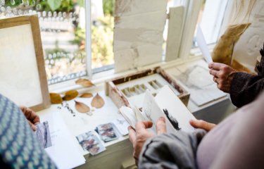 A close up of hands looking through sketchbooks and artworks on a table