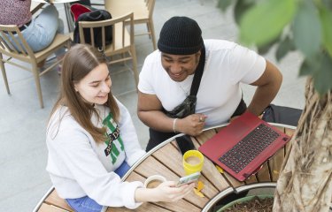 Two students sitting at a table with a laptop and drinks