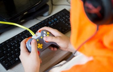 Hands holding a gaming controller in front of a computer keyboard