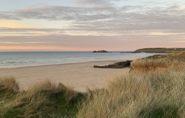 Godrevy beach with grass in the foreground and the sun setting in the background