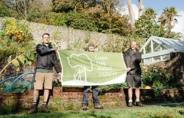 Three people holding up a banner in gardens