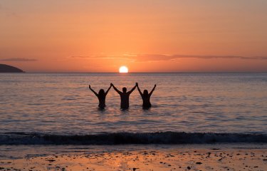 Three Falmouth University students in the sea as the sun is setting