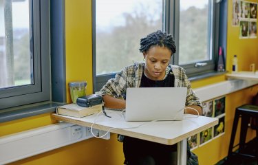 A student sat at a table with a laptop and yellow walls