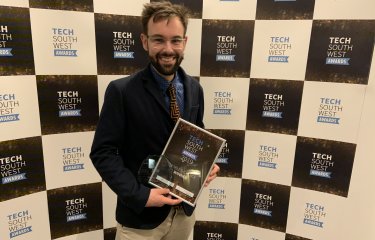 Lecturer holding the Tech South West Award, with a backdrop with branding on it.