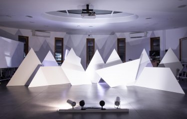 White triangle sculptures in a room lit with purple light