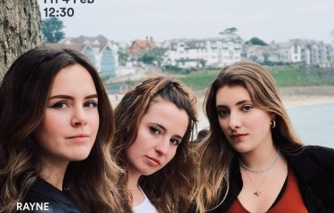 The members of Rayne stand together in front of a beach