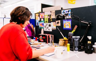 Falmouth University Illustration student wearing a red jumper and drawing at a desk