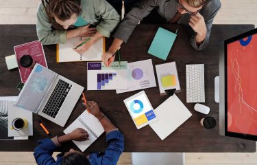 Three people sat at a table with graphs on paper