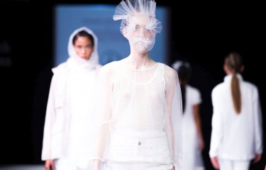 Models on a catwalk wearing white clothing and a netted face mask