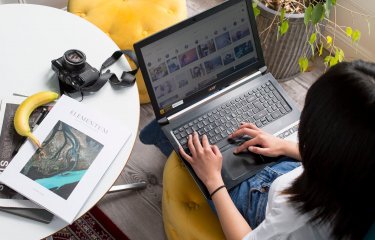 A student working on a laptop next to a white table with a camera and magazine