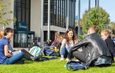 Penryn campus students outside exchange, sitting on grass