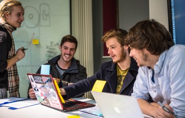 Falmouth University Business students smiling and looking at a laptop