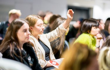 Female student raising hand in a crowd