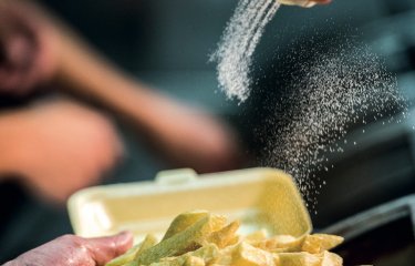 A hand pouring salt on a portion of chips