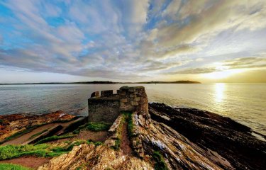 Ruins of a castle on a cliff with the sea and sun in the background