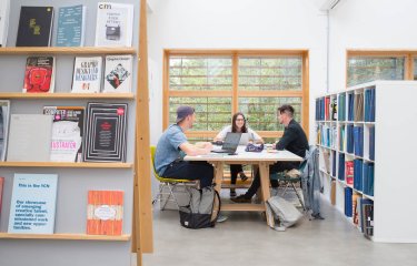 Three students sat at a table in a Graphic Design studio at Falmouth University