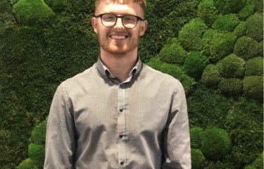 Will Dorrell Business and Entrepreneurship graduate standing in front of green moss wall.