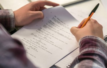 Hands holding a script and annotating it with a pen