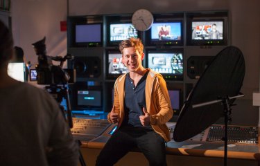 Student giving the thumbs up in television control studio.