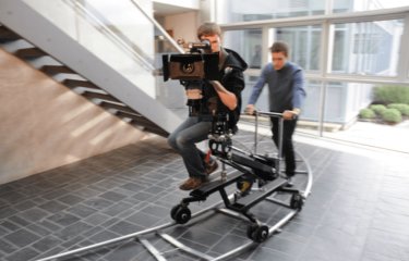 Student behind camera on camera dolly being moved along a track.