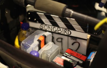 Close up of filming equipment, clapperboard with the word Songbird on it.